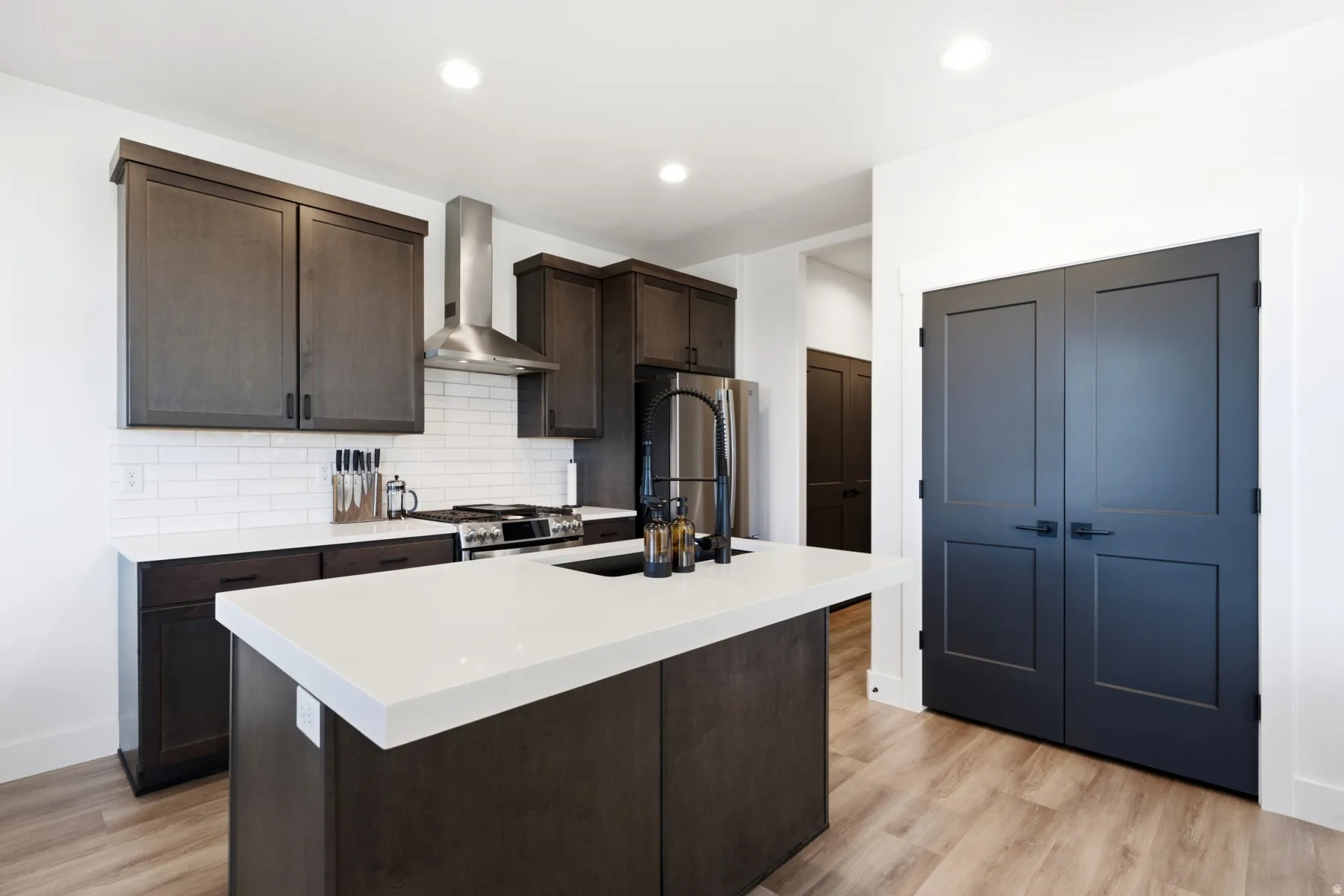 Kitchen featuring dark wood-finish cabinetry, white subway tile backsplash, stainless steel appliances, a center island with a white countertop, and wood-finish flooring