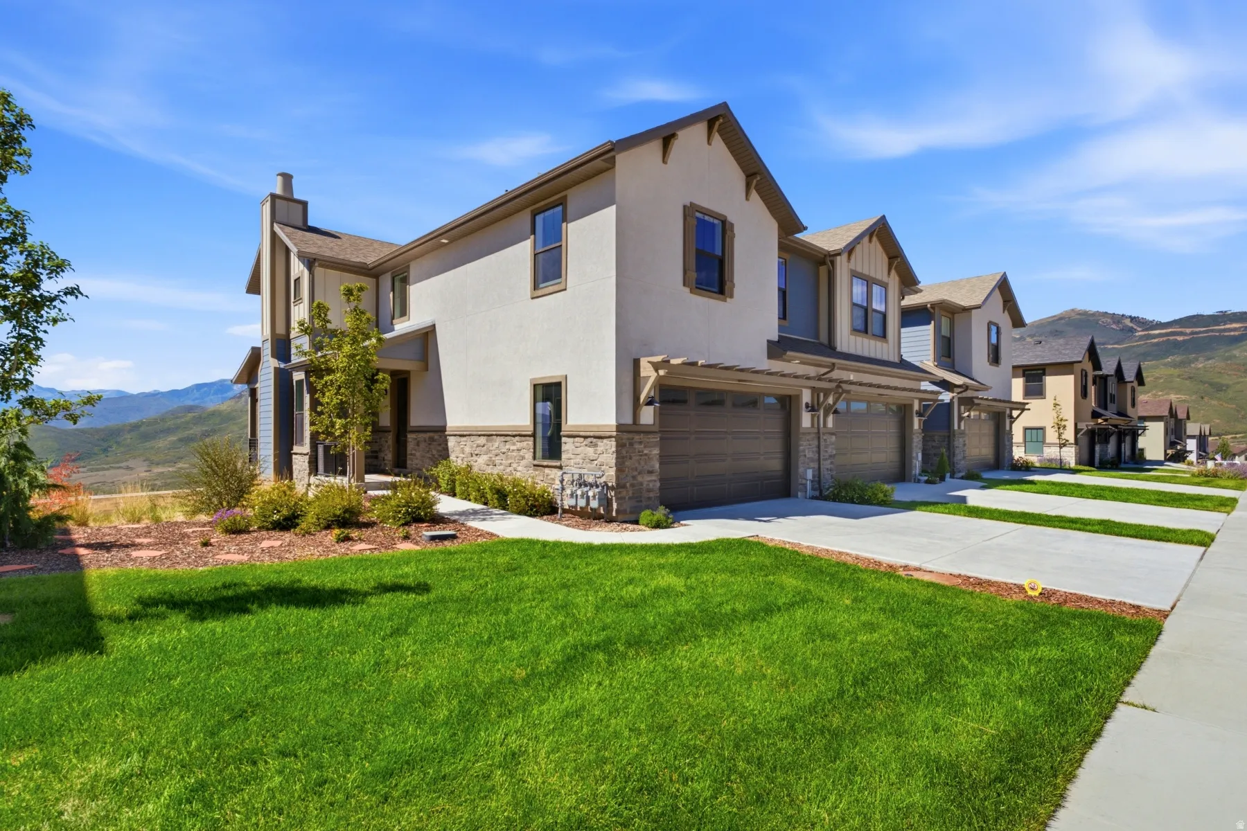Multi-level residence featuring a stucco and stone veneer exterior, a two-car garage with a pergola, and a concrete driveway