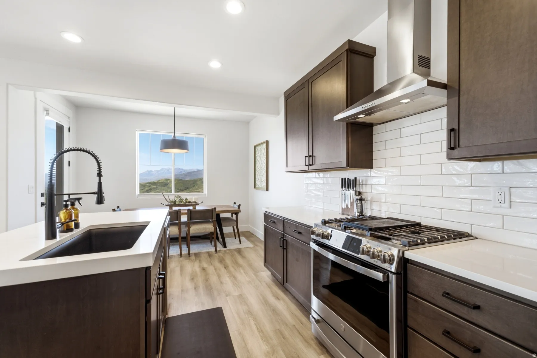 Dark wood-finish cabinetry with matte black hardware, stainless steel appliances, white subway tile backsplash, white countertops, and wood-finish flooring
