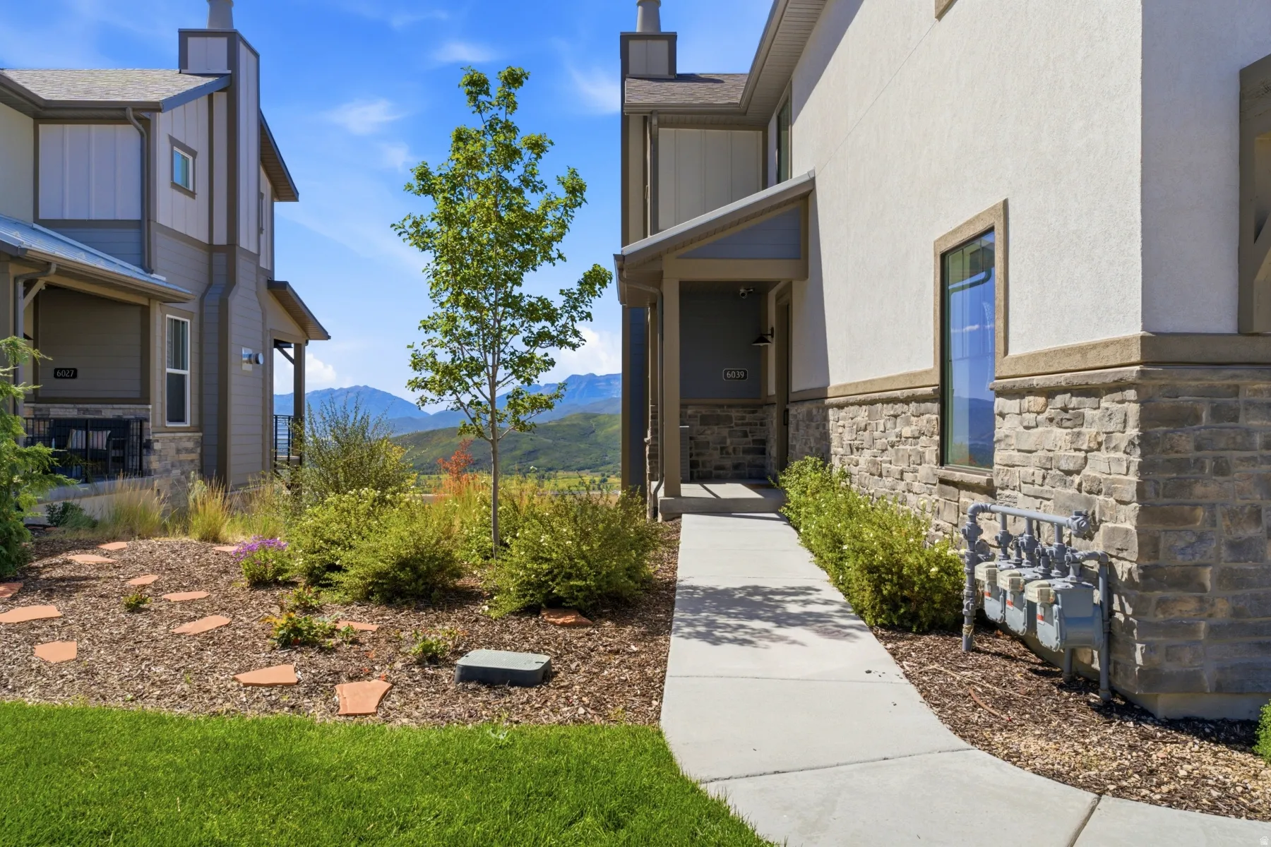Stucco and stone exterior with covered entry, concrete walkway, and landscaped garden area