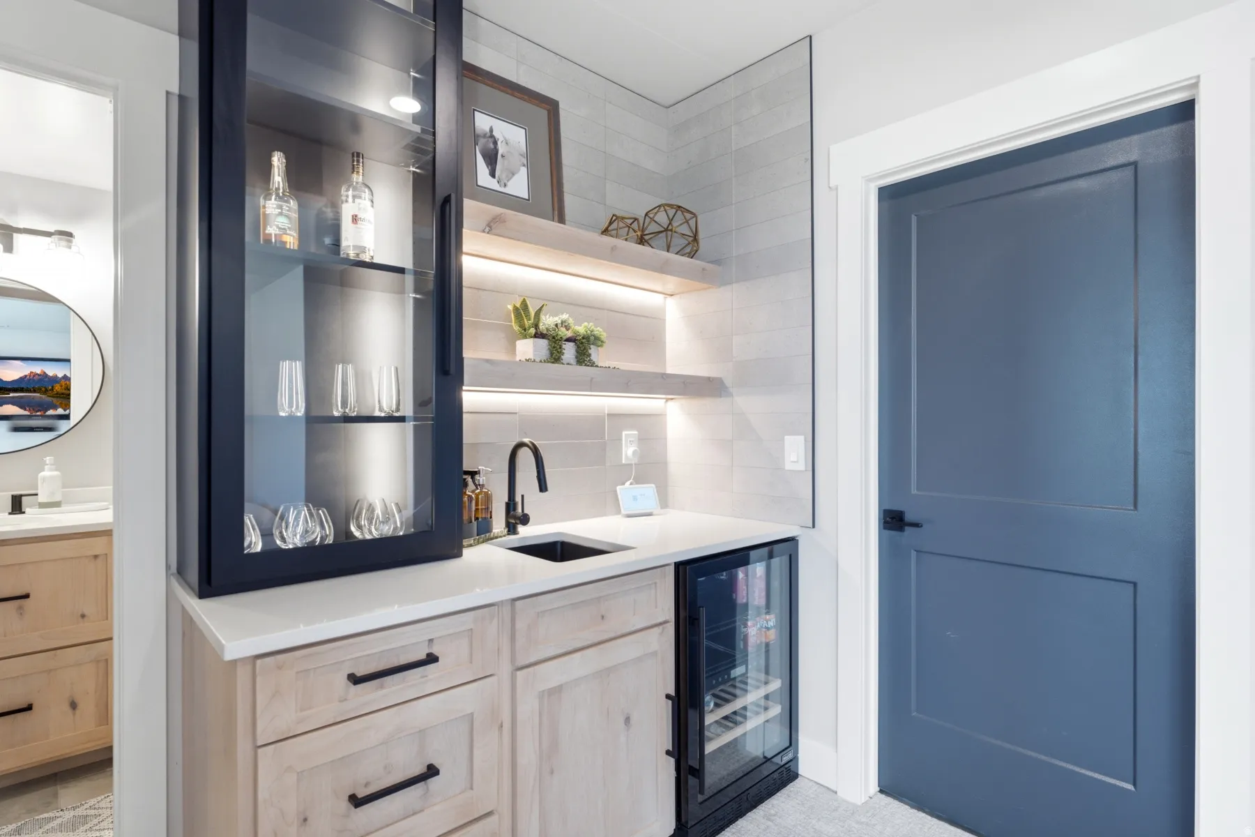 Custom built-in cabinetry with glass-front upper storage, undermount sink, beverage refrigerator, and light wood-finish lower cabinets