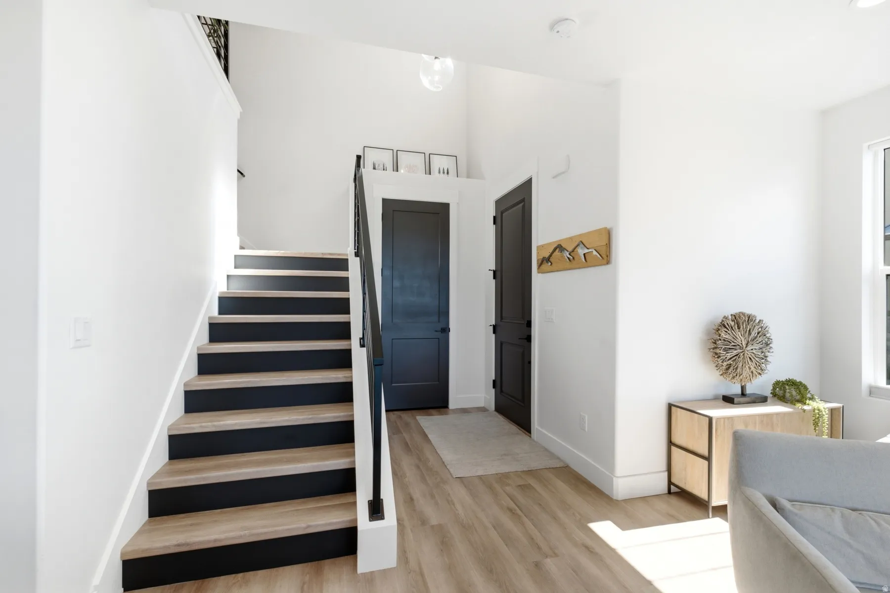 Light wood-finish flooring, staircase with black risers, black handrail, high ceilings, and recessed lighting