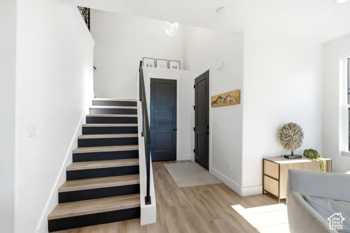 Light wood-finish flooring, staircase with black risers, black handrail, high ceilings, and recessed lighting