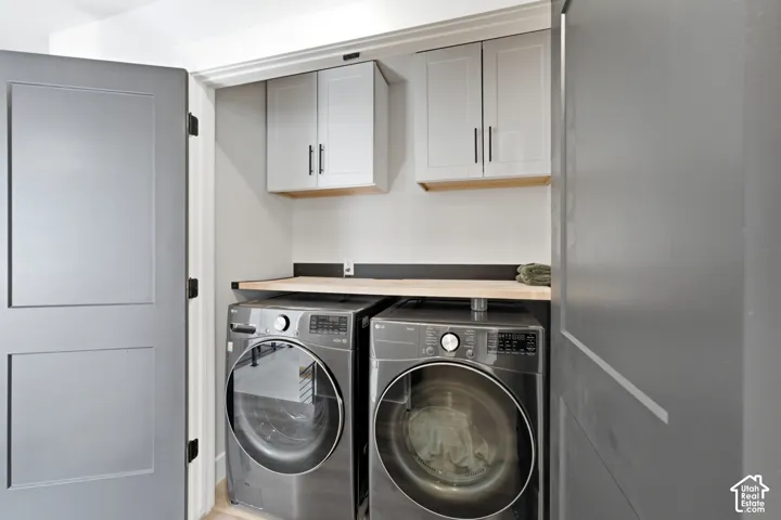 Dedicated laundry area featuring a light wood finish countertop, two upper cabinets with black hardware, and two front-loading machines