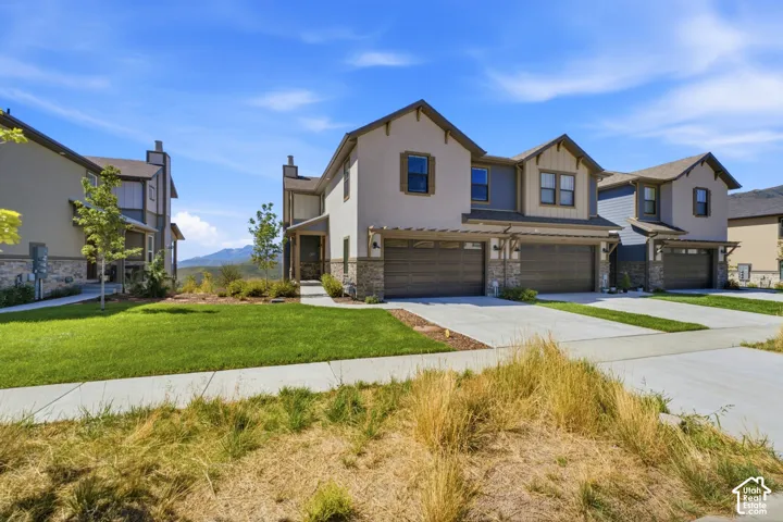 Stucco exterior with stone accents, attached two-car garage, covered entry, and landscaped front yard