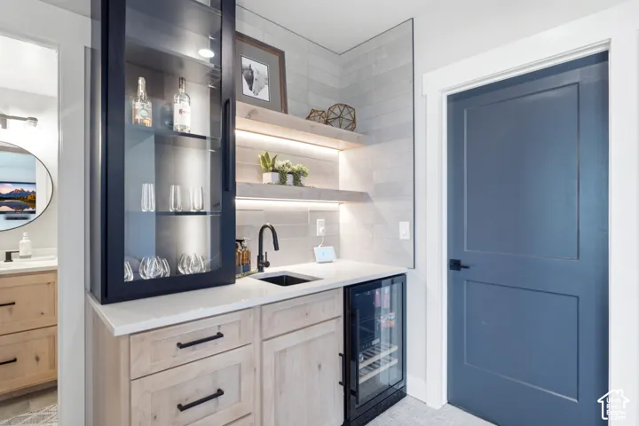 Custom built-in cabinetry with glass-front upper storage, undermount sink, beverage refrigerator, and light wood-finish lower cabinets