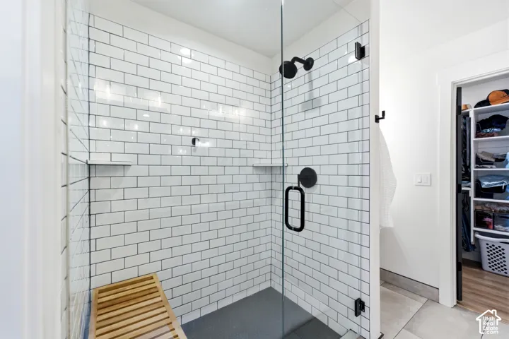 Walk-in shower featuring white subway tile, a dark-toned shower pan, and matte black fixtures