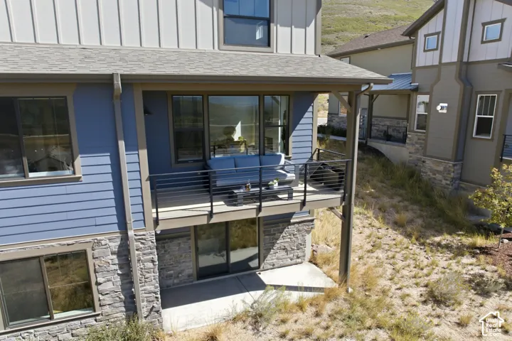 Exterior with blue horizontal siding, stone veneer accents, an upper-level deck with horizontal railing, and a ground-level concrete patio