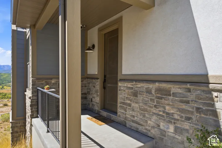 Entryway featuring stone facade, stucco exterior, covered porch, and mountain backdrop