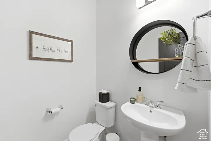 Pedestal sink with chrome faucet, wall-mounted circular mirror with integrated wood-finish shelf, and polished chrome towel bar