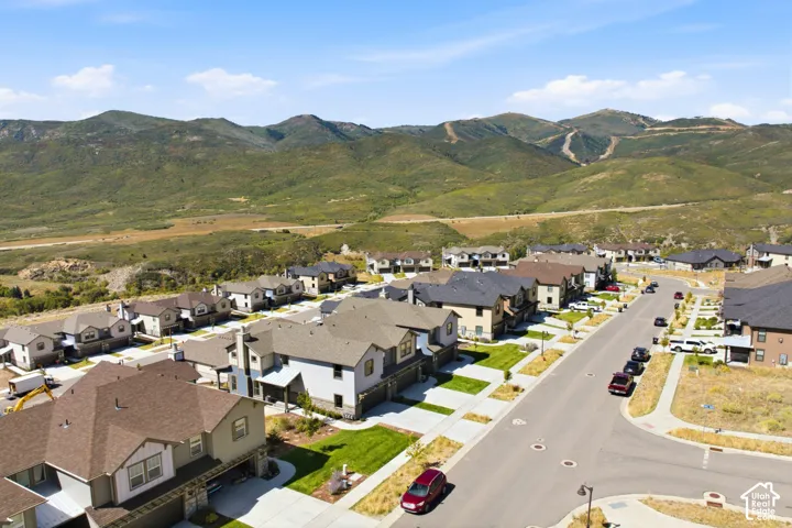 Residential neighborhood with paved streets and sidewalks, featuring multiple single-family homes with varying exterior finishes, against a backdrop of natural mountainous terrain