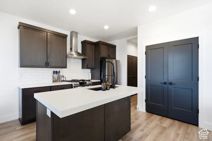 Kitchen featuring dark wood-finish cabinetry, white subway tile backsplash, stainless steel appliances, a center island with a white countertop, and wood-finish flooring