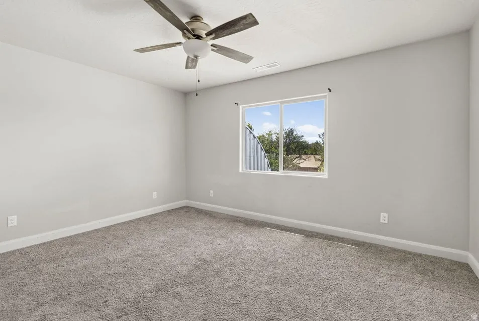 Neutral wall color, ceiling fan with light, large window, and carpeted flooring