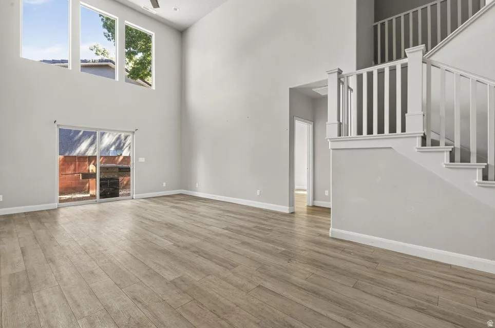 Vaulted ceiling, wood-finish flooring, sliding glass door, white trim, and a staircase with white railings
