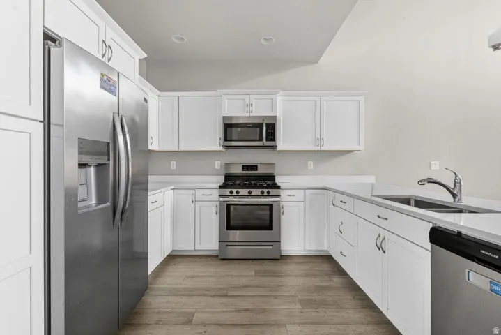Kitchen featuring stainless steel appliances, white cabinetry, light-toned countertops, a double basin sink, and wood-finish flooring