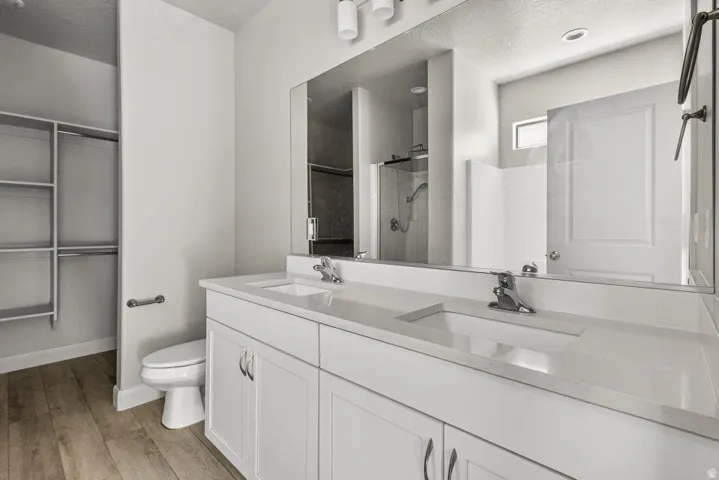 Dual vanity with integrated sinks, wood-finish flooring, built-in shelving, glass-enclosed shower, and a large wall-mounted mirror