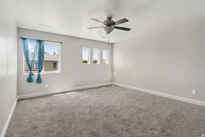 Spacious room featuring neutral carpeting, light-toned walls, multiple windows providing natural illumination, and a ceiling fan