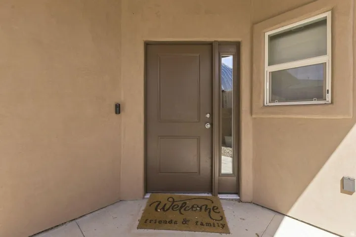 Stucco exterior featuring a panel-style entry door with a sidelight, an exterior wall light, and a single-hung window with white framing