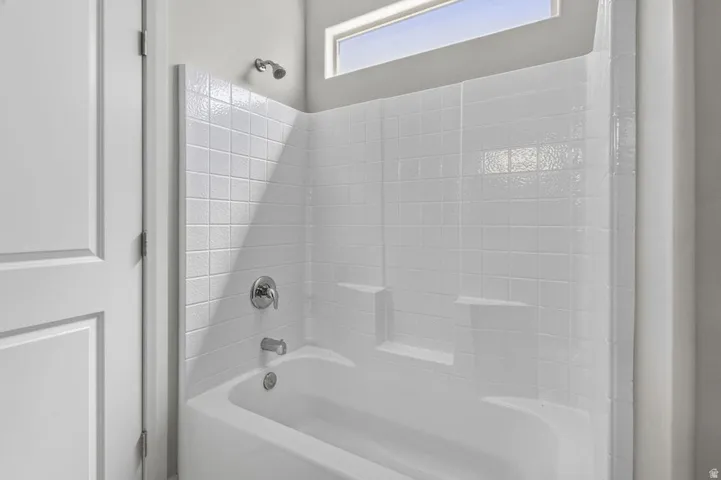 Bathtub with integrated shelving, white tile-patterned surround, chrome fixtures, and a transom window