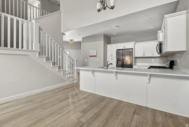 Wood-finish flooring, white cabinetry, stainless steel appliances, white countertops, and a white staircase