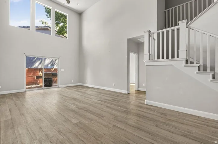 Vaulted ceiling, wood-finish flooring, sliding glass door, white trim, and a staircase with white railings