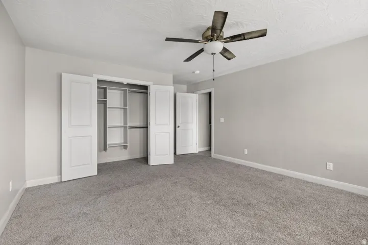Plush gray carpeting, light gray wall paint, white trim, and a ceiling fan with integrated lighting