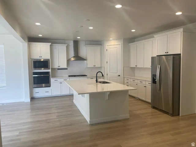 Modern kitchen featuring white shaker cabinetry, stainless steel appliances, a large center island with a sink, quartz countertops, and wood-finish flooring