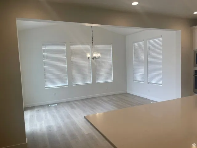 Open concept living space featuring light wood-finish flooring, recessed lighting, a vaulted ceiling, and multiple windows with blinds