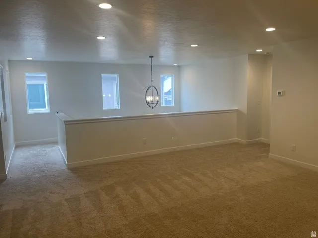 Spacious carpeted area featuring recessed lighting, a decorative chandelier, and multiple windows