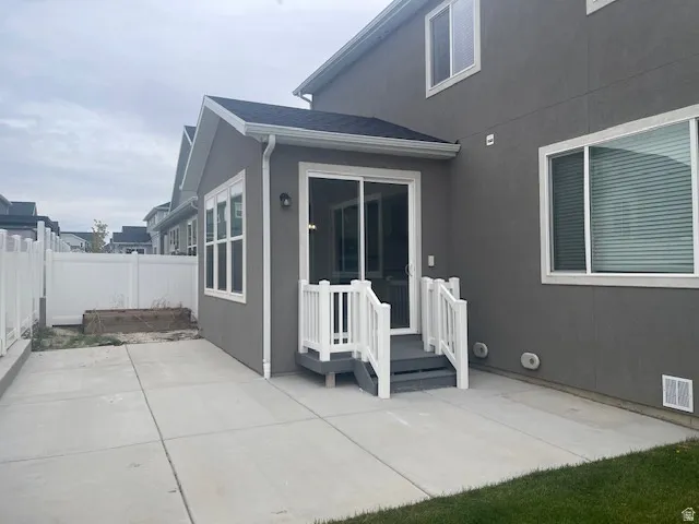 Rear exterior with concrete patio, white vinyl fencing, sliding glass door, and exterior lighting