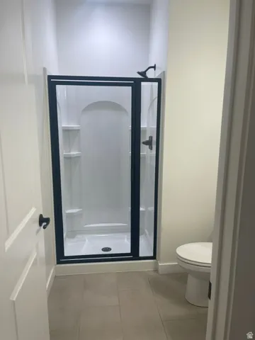Shower enclosure with dark-framed glass door, built-in shelving, white shower surround, and tile flooring
