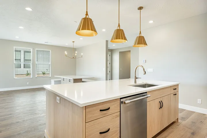 Kitchen island with a white countertop and integrated stainless steel sink, brass pendant lighting, wood-finish cabinetry with black hardware, and wood-finish flooring throughout