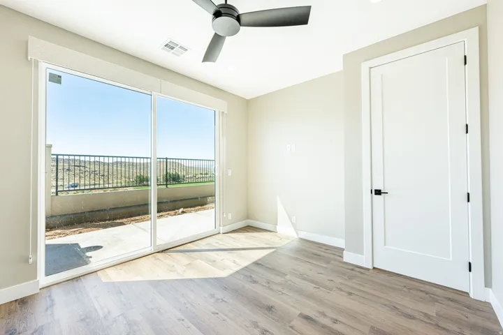 Sliding glass door leading to a concrete patio, wood-finish flooring, white interior door with black hardware, and a ceiling fan