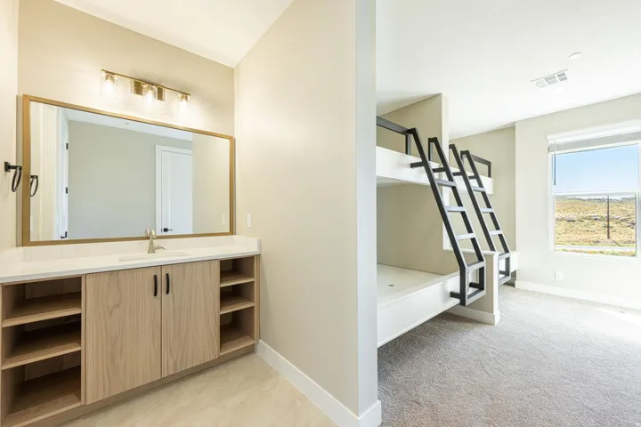 Built-in bunk beds with black metal ladders, a vanity with a light wood-finish cabinet, a large framed mirror, a single basin sink, and a window with a roller shade