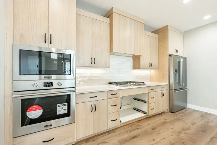 Light wood-finish cabinetry, stainless steel appliances, white subway tile backsplash, white countertops, and wood-finish flooring