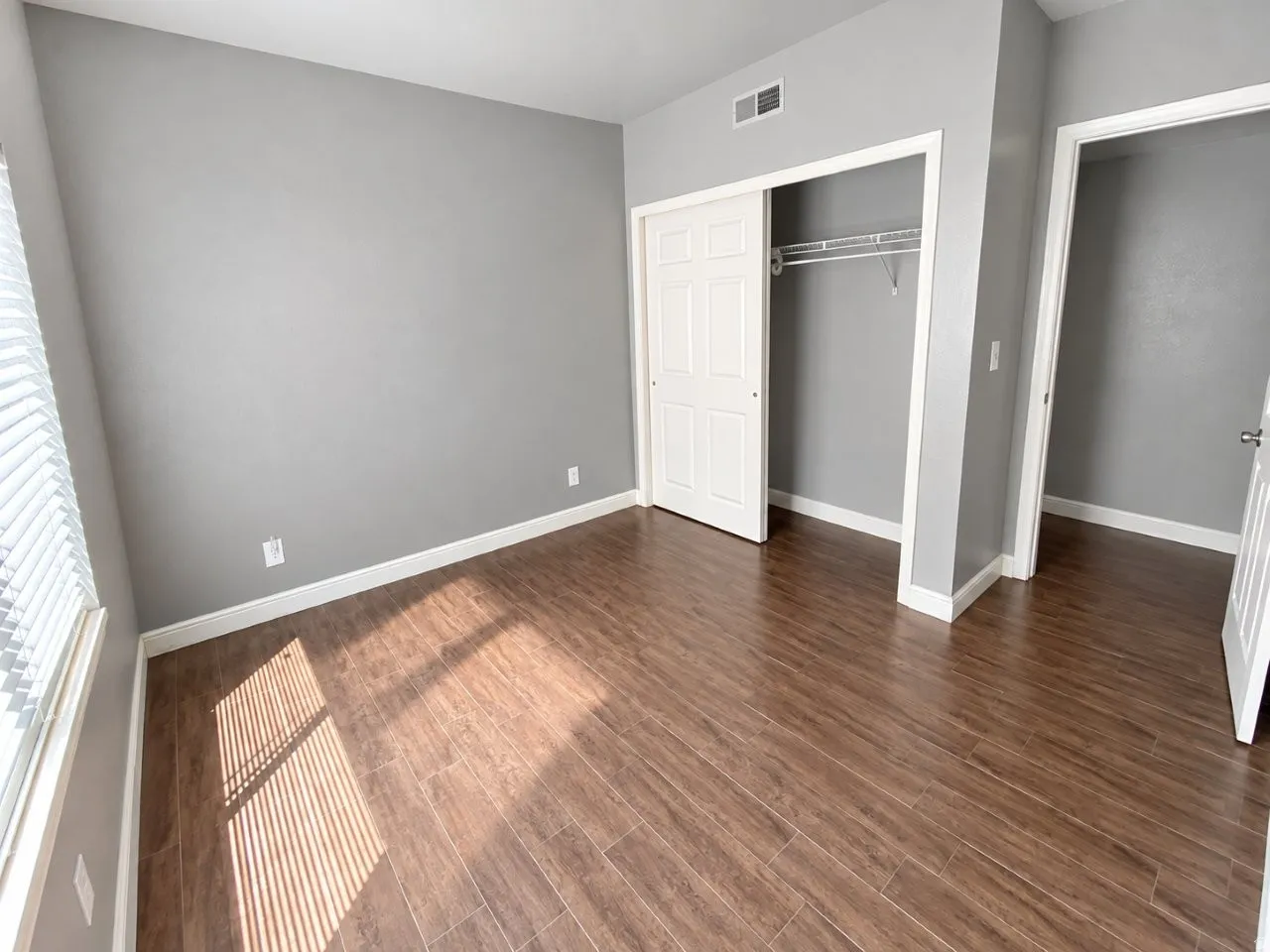 Wood-finish flooring, neutral gray wall tones, white trim, and a built-in closet with sliding doors