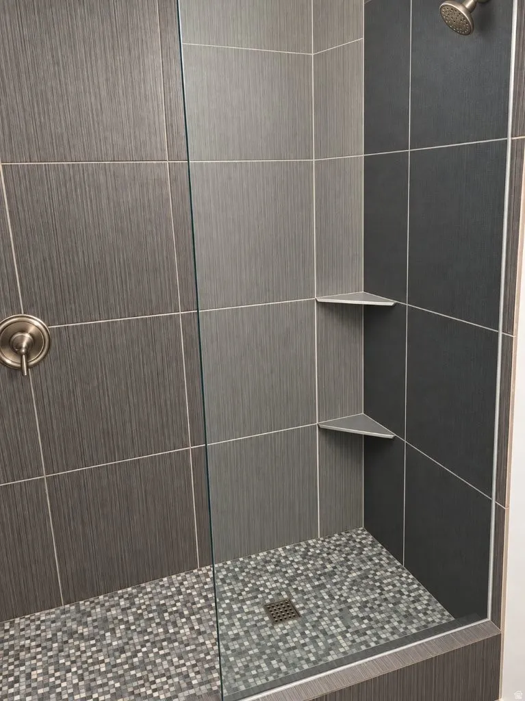Glass-enclosed shower featuring a textured tile surround, mosaic tile flooring, built-in corner shelving, and a brushed nickel showerhead and control
