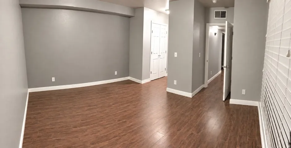 Wood-finish flooring, light grey wall paint, white trim, white window blinds, and white bi-fold closet doors