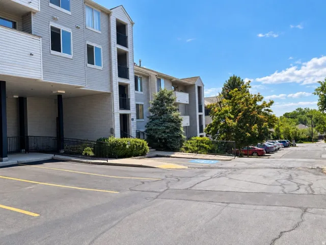 Multi-level building with light-toned siding, multiple balconies, and an integrated covered parking area