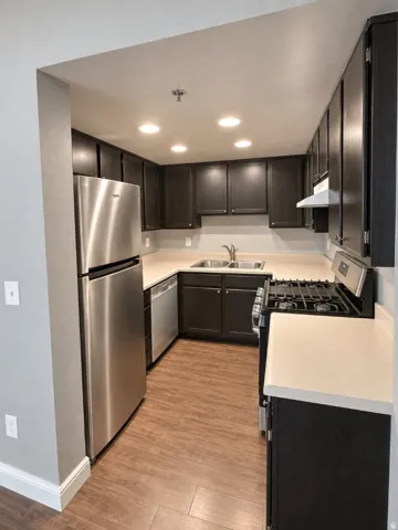 Kitchen featuring dark wood-finish cabinetry, white countertops, stainless steel appliances, wood-finish flooring, and recessed lighting