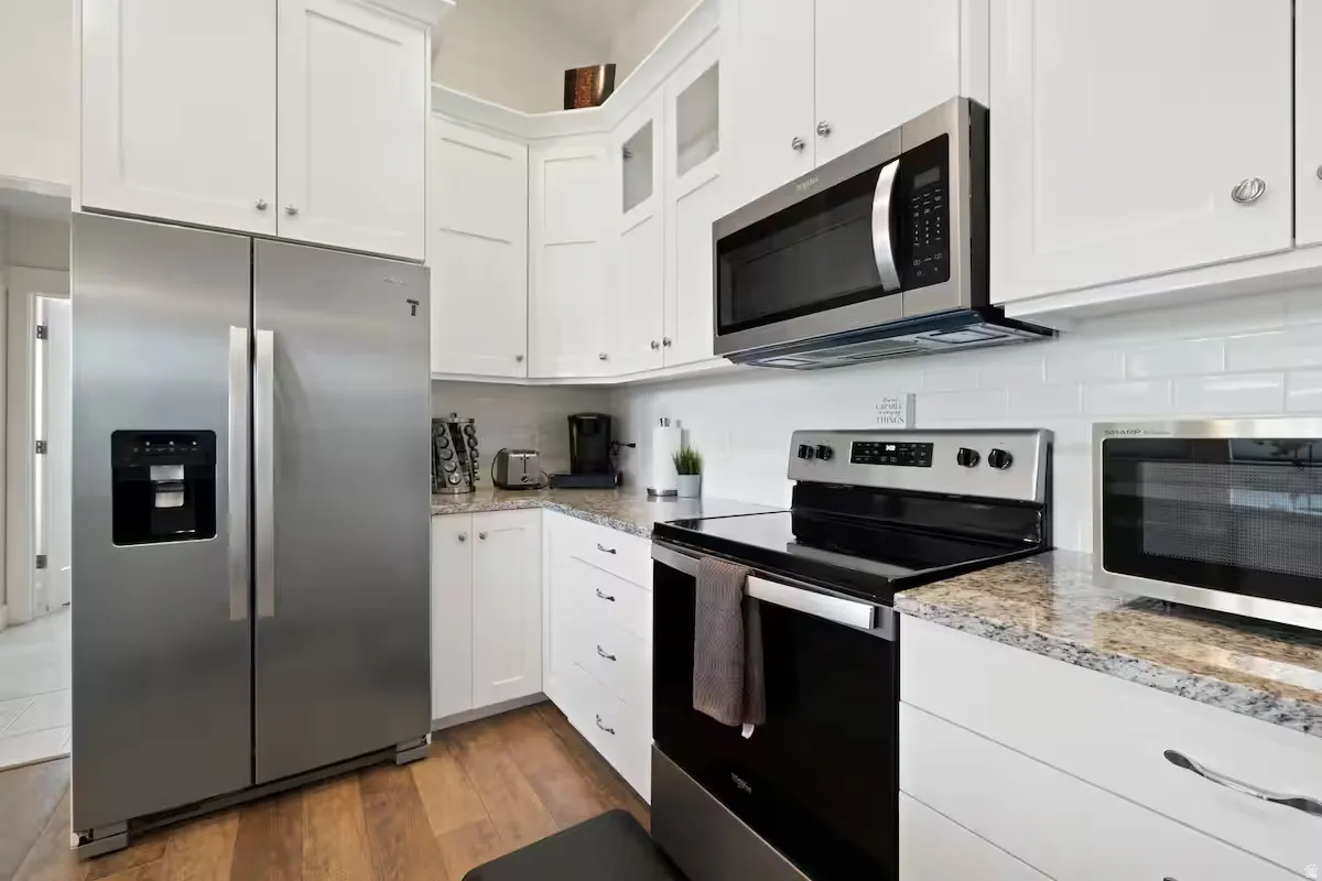 White shaker cabinetry, stainless steel appliances, granite countertops, subway tile backsplash, and wood-finish flooring