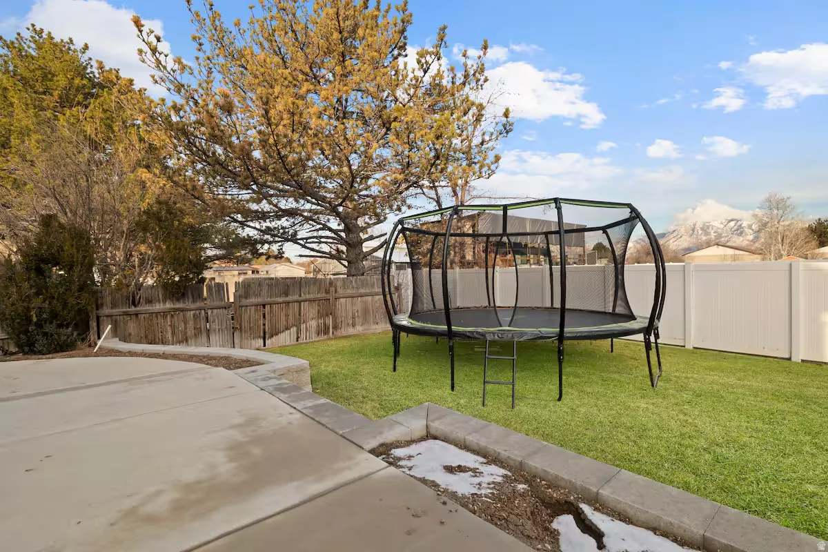 Expansive concrete patio with a retaining wall, surrounded by a manicured lawn and mature trees