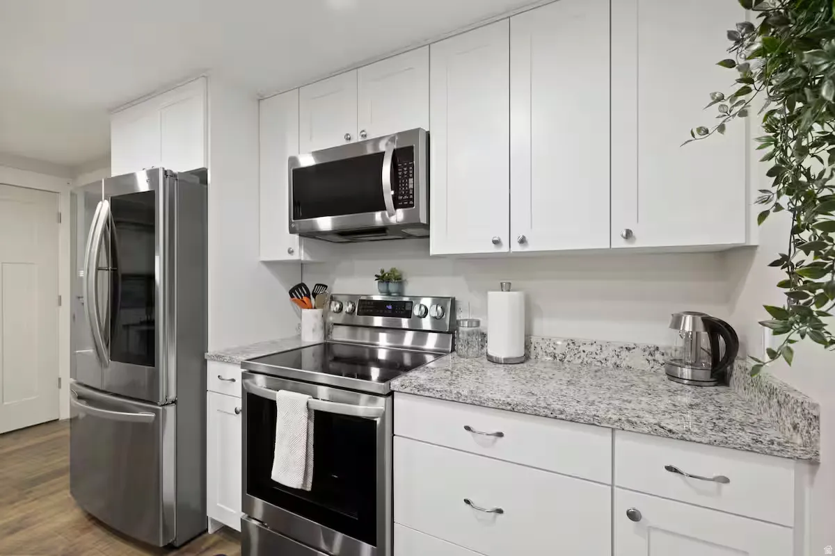 White cabinetry with brushed nickel hardware, stainless steel appliances, speckled stone countertops, and wood-finish flooring