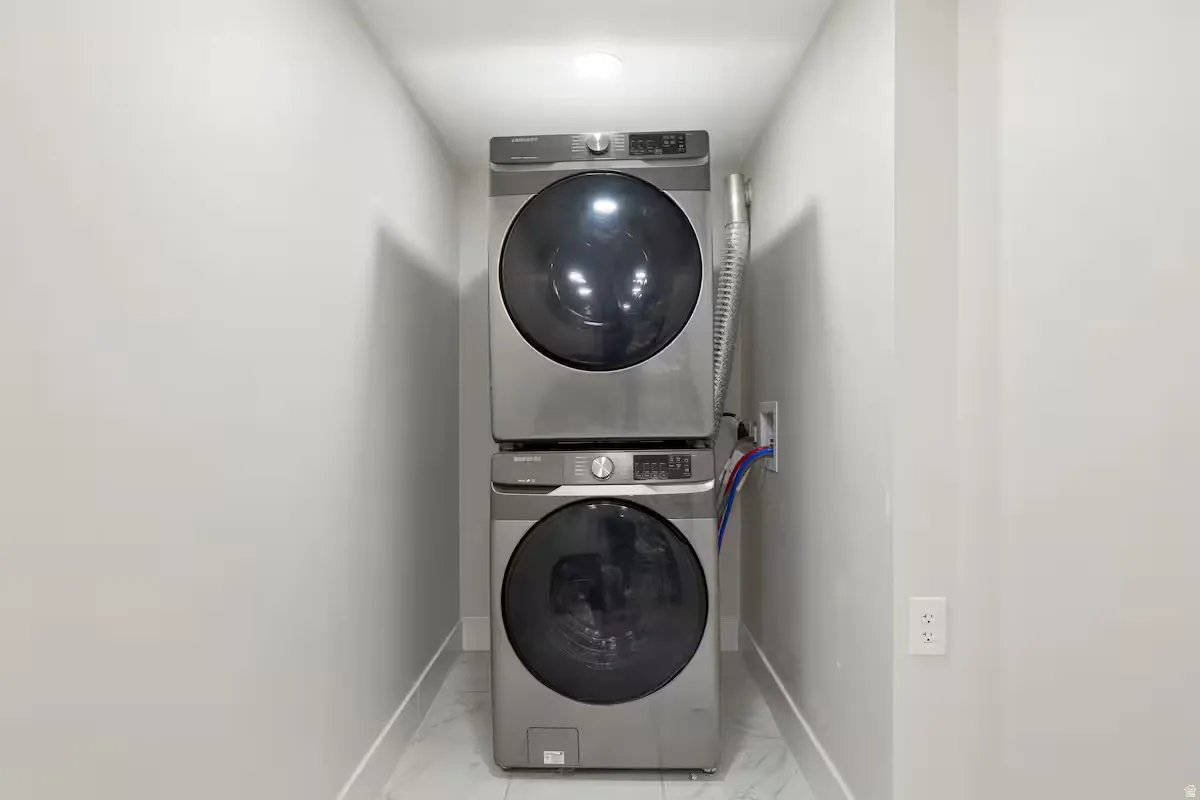 Laundry area featuring a stacked washer and dryer, recessed ceiling lighting, and tile flooring