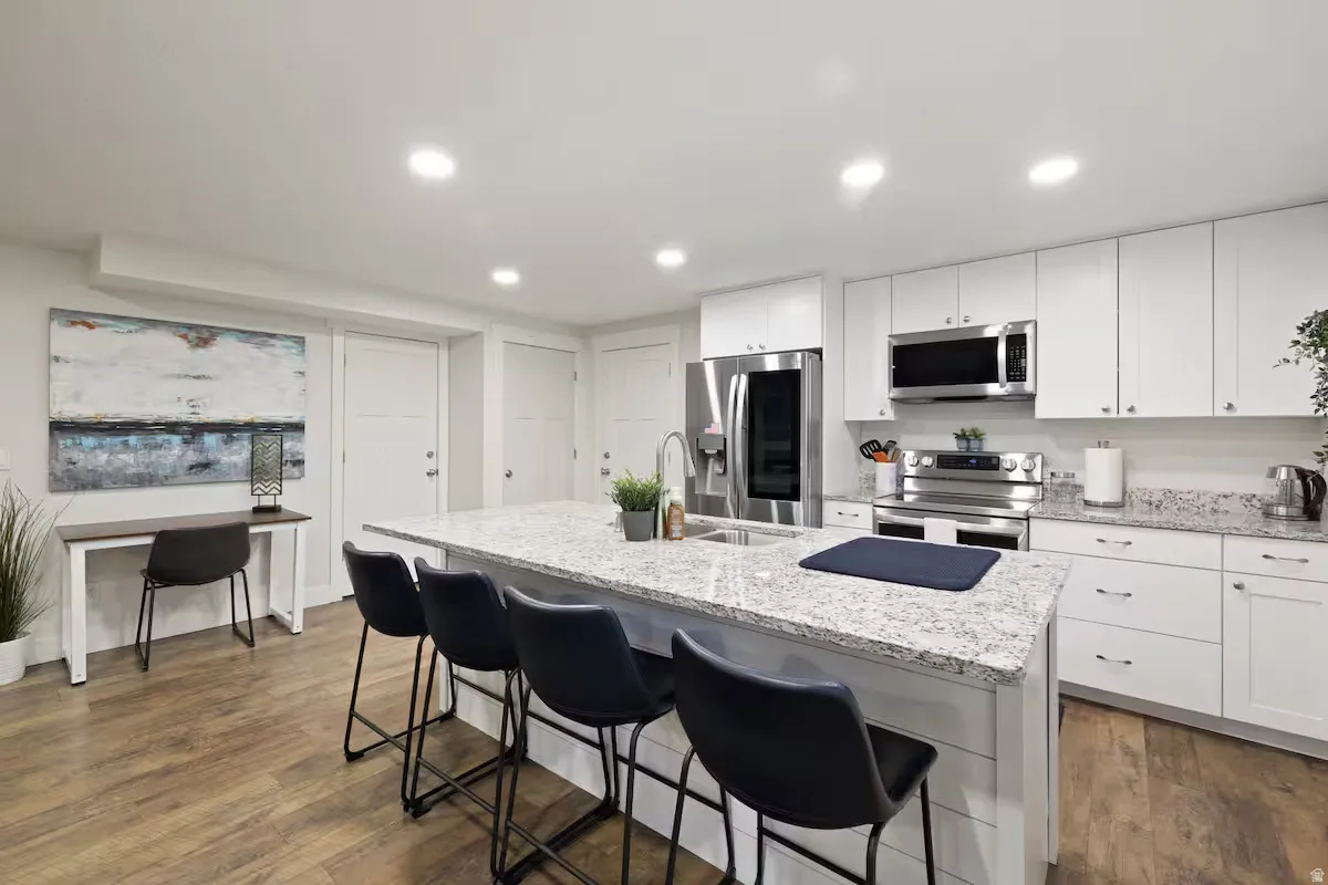Kitchen featuring wood-finish flooring, white cabinetry, granite countertops, stainless steel appliances, and a central island with seating