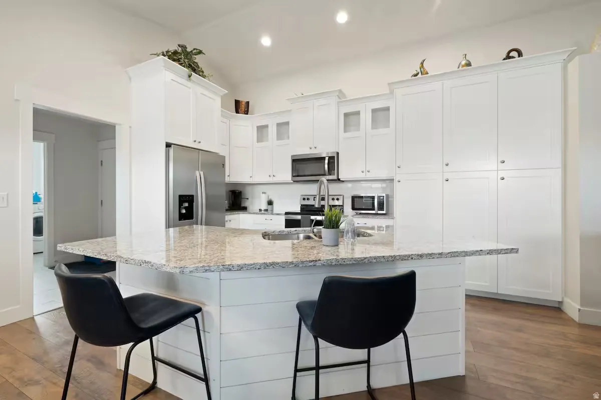 Kitchen featuring white cabinetry, stainless steel appliances, a multi-tone countertop, and wood-finish flooring