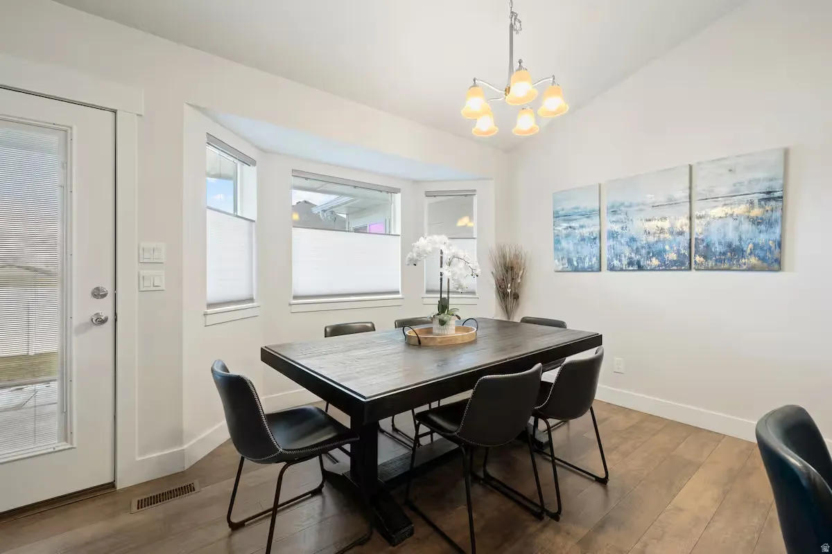 Vaulted ceiling featuring a chandelier, wood-finish flooring, bay window, and a glass-paneled exterior door
