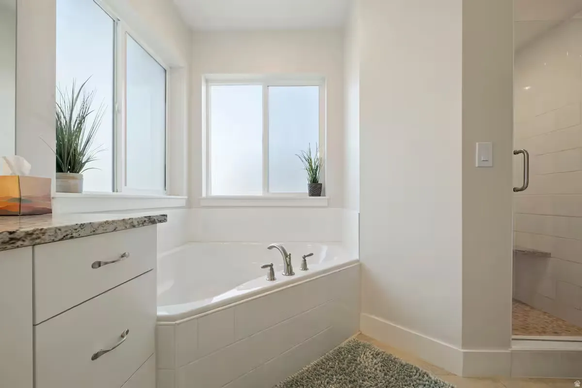 White corner soaking tub with deck-mounted fixtures, adjacent to a vanity with a stone countertop and white cabinetry