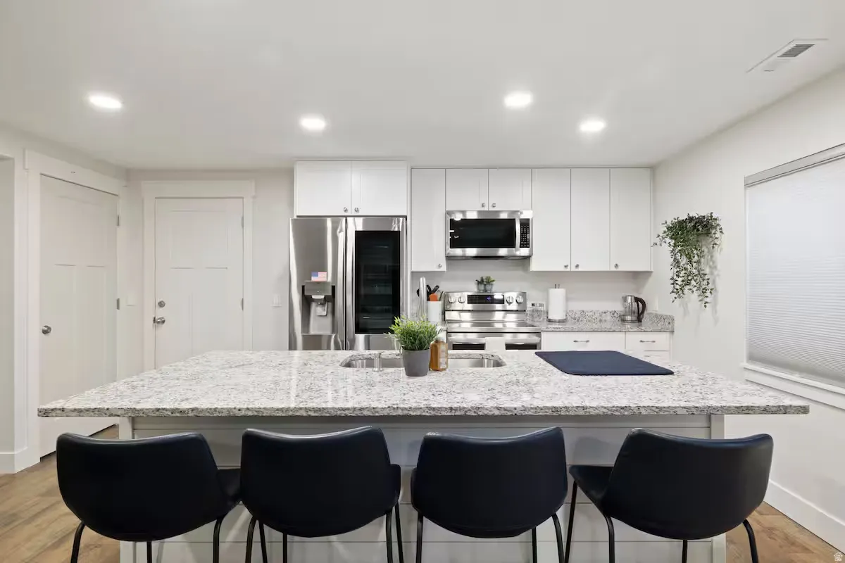 Kitchen featuring a large island with an integrated sink, white cabinetry, stainless steel appliances, and wood-finish flooring