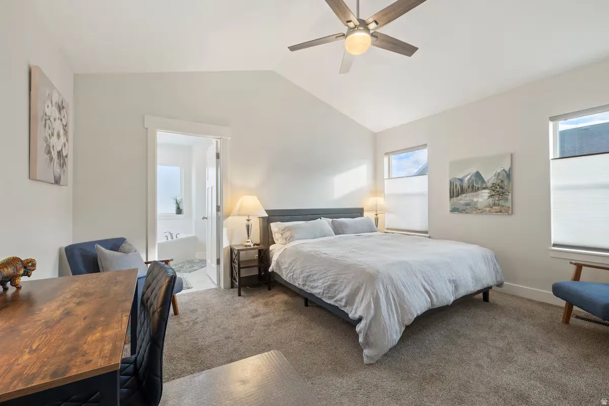 Vaulted ceilings, a built-in ceiling fan, light gray carpeting, and a white soaking tub